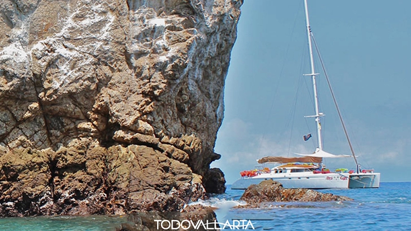 Ally Cat cruising past a rocky reef formation near Los Arcos during a catamaran charter 56.
