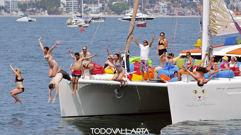 Group of sun-kissed guests diving off Ally Cat’s netted bowsprit into Banderas Bay on a catamaran charter 56.