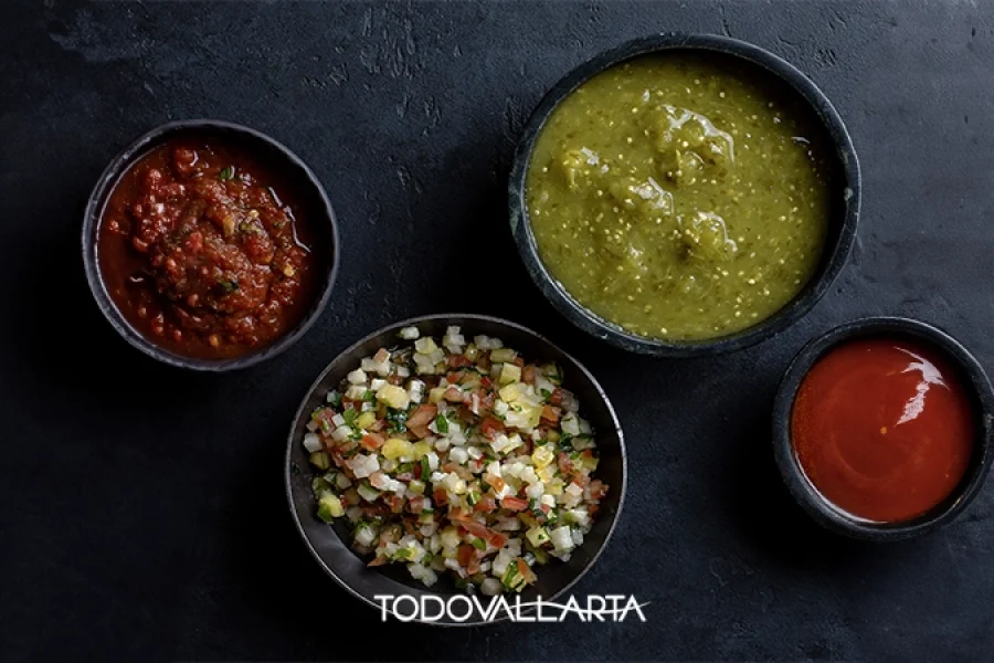 A selection of traditional Mexican salsas, including red, green, and pico de gallo, displayed in black bowls on a dark background.