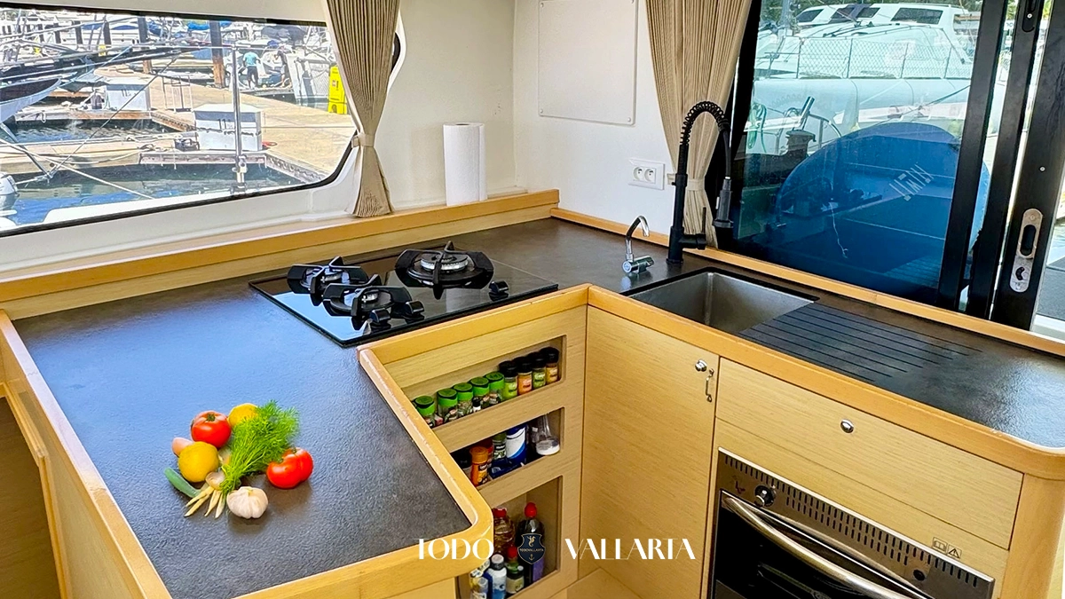 charter goa - 42Ft luxury catamaran galley with black countertop, two-burner stove, sink, and fresh produce